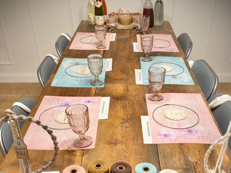 Tisch gedeckt mit rosa und blauen Platzdeckchen, Gläsern und Geschirr und Bastelmaterial