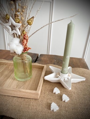 Weißer Kerzenhalter in Sternform mit grüner Kerze und einer grünen Glasvase mit Trockenblumen 