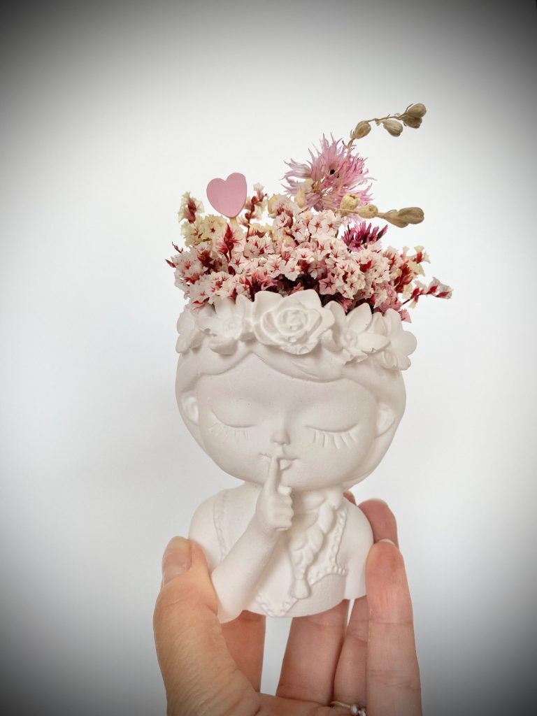 Weißer Mädchenkopf mit Trockenblumen und Herzen als Dekoration in einer Hand gehalten.