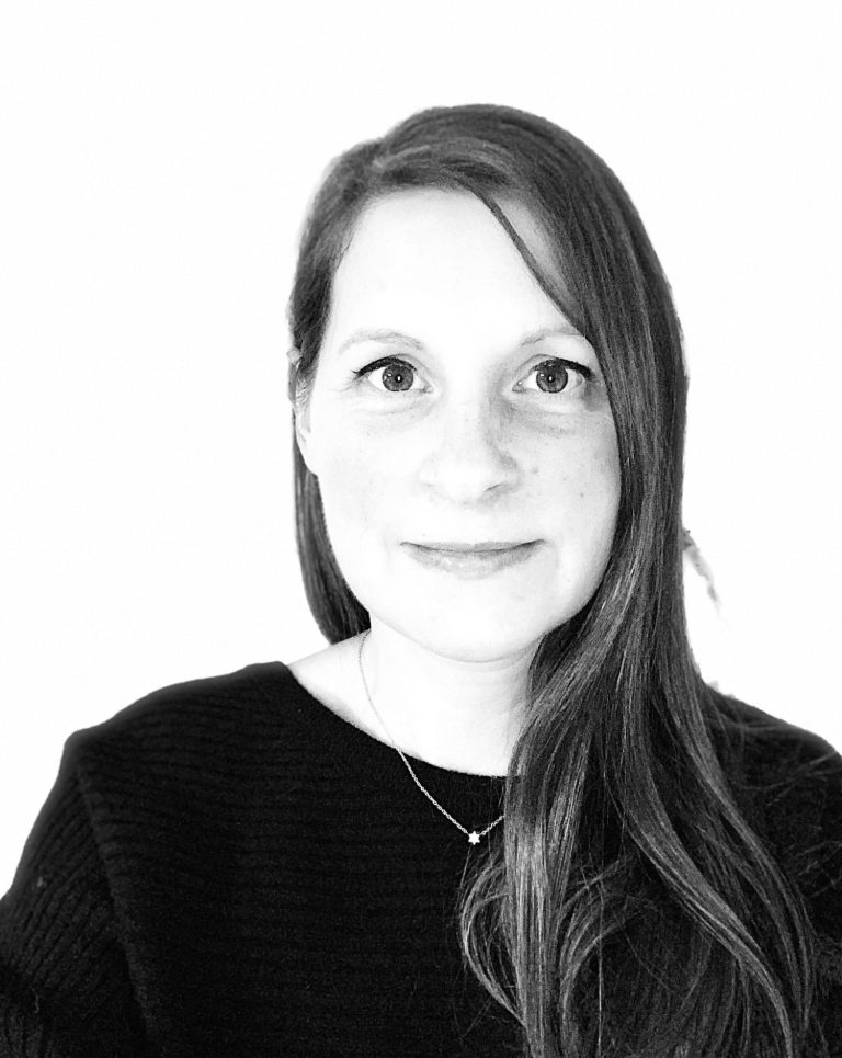 Porträt einer Frau mit langen, braunen Haaren und einem tiefschwarzen Pullover.