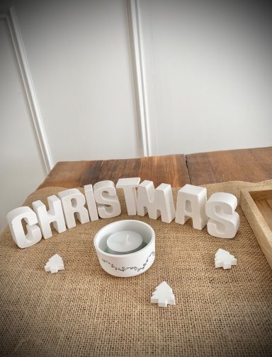 Weiße Buchstaben die das Wort Christmas ergeben und ein Teelichthalter mit weißem Teelicht