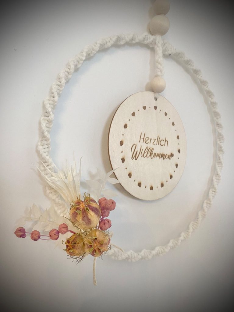 Ein hängender Kranz aus Seil mit einer Holzscheibe und getrockneten Blumen.